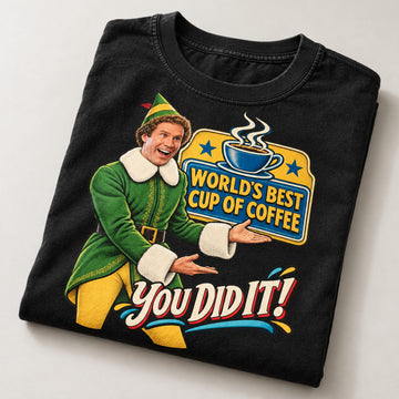 World's Best Cup of Coffee Elf Christmas T-Shirt, folded on a warm grey backdrop