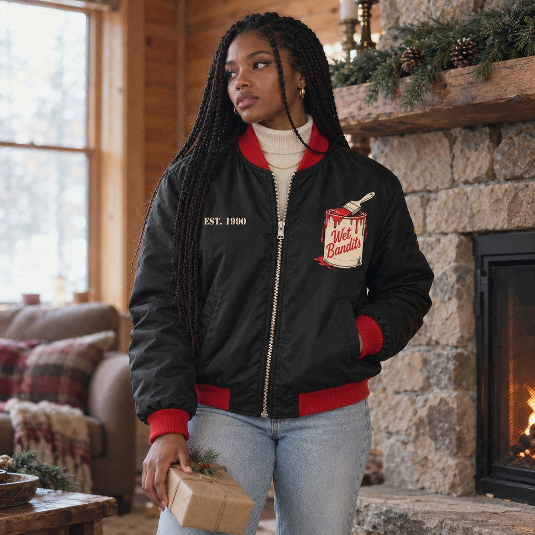 Woman by a stone fireplace wearing the Wet Bandits paint can bomber jacket
