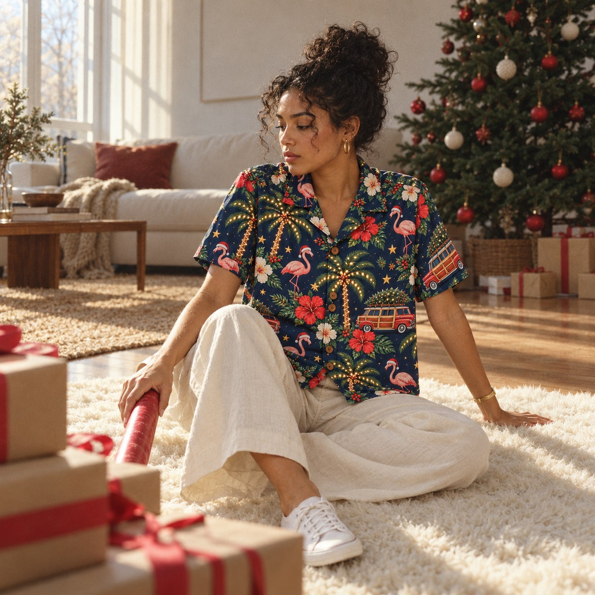 Woman in a Christmas flamingo Hawaiian shirt sitting on a white rug beside wrapped gifts