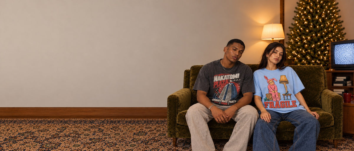 Two models in holiday movie graphic tees on a green velvet sofahero-slide