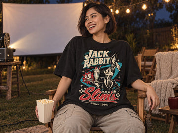 Woman in a black Jack Rabbit Slim's graphic tee laughing at a backyard outdoor movie night with a projector and string lights