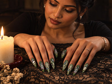 Hands wearing dark green Haunted Garden press-on nails resting on black lace by candlelight