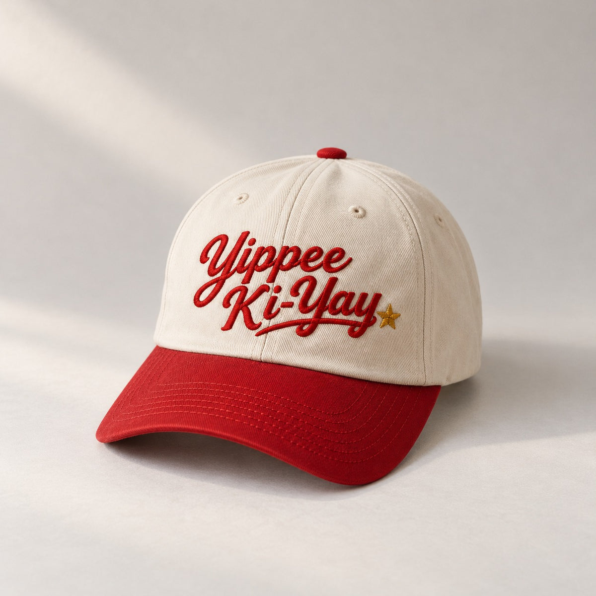 Cream baseball cap with a red brim and red embroidered Yippee Ki-Yay script with a gold star