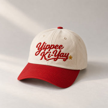Cream baseball cap with a red brim and red embroidered Yippee Ki-Yay script with a gold star