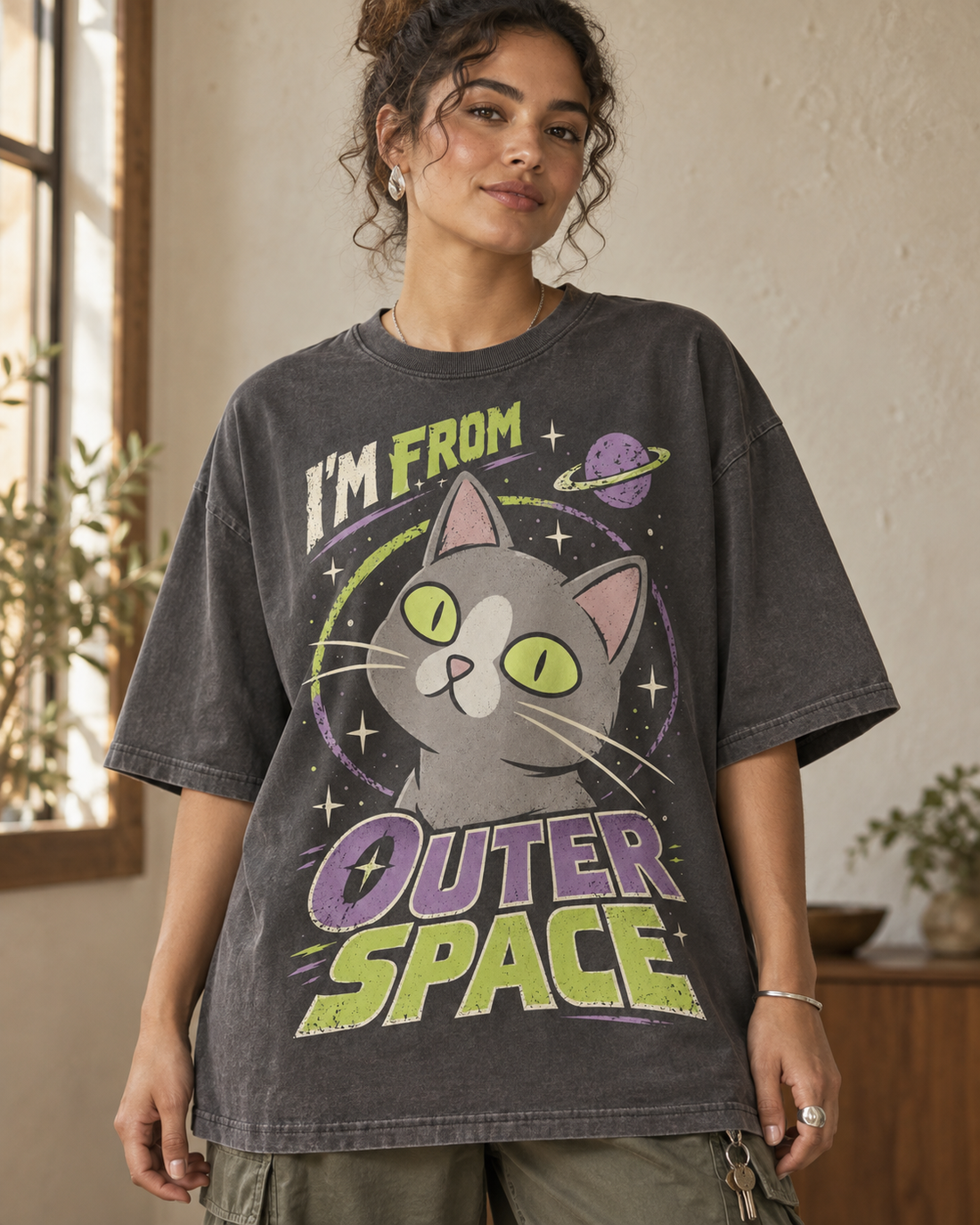 Mockup of a black Outer Space Cat graphic T-shirt with retro lettering and cream, lime and purple cat artwork.